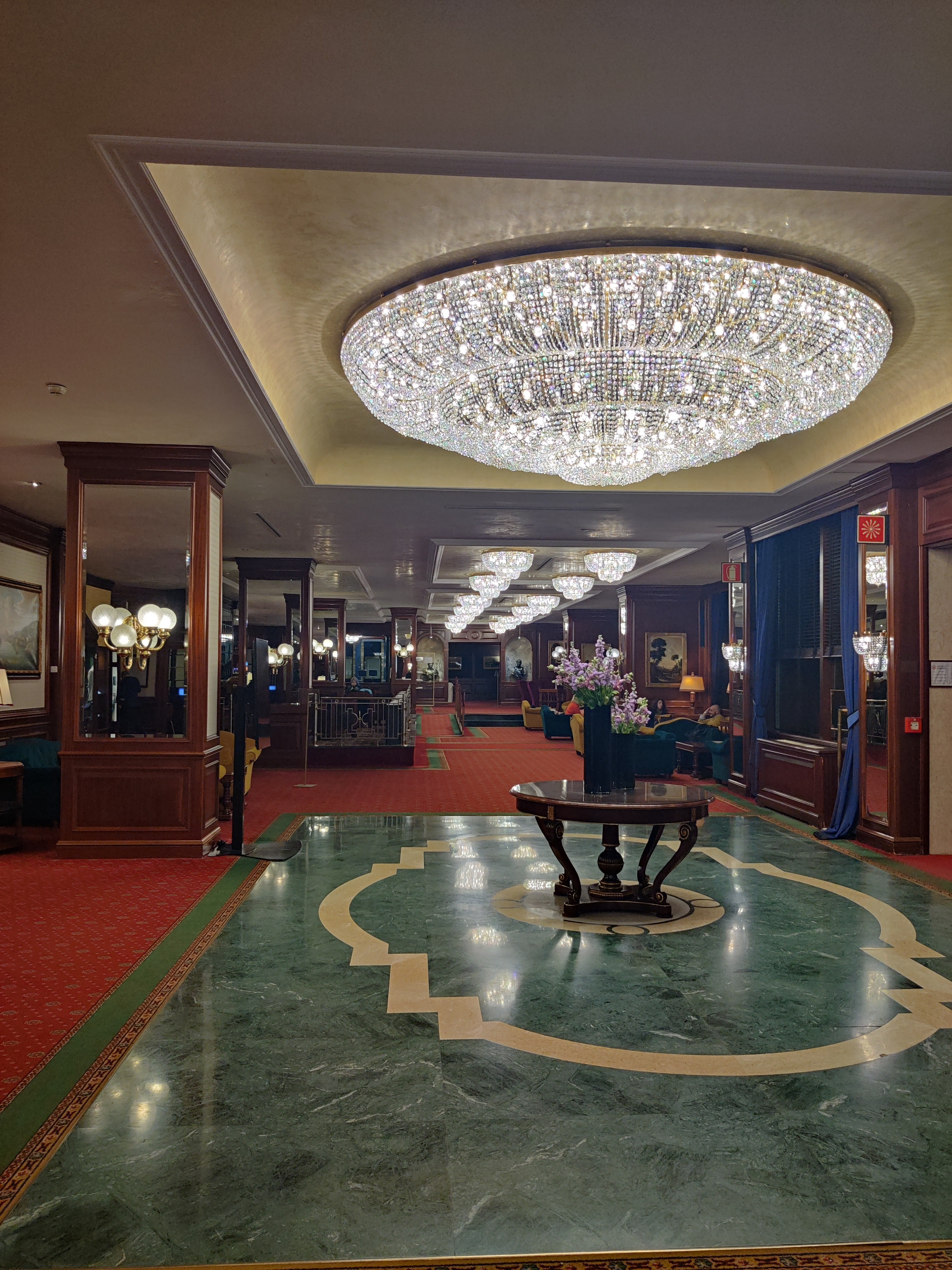 Grand hotel lobby in Bologna with a massive crystal chandelier and green marble floor