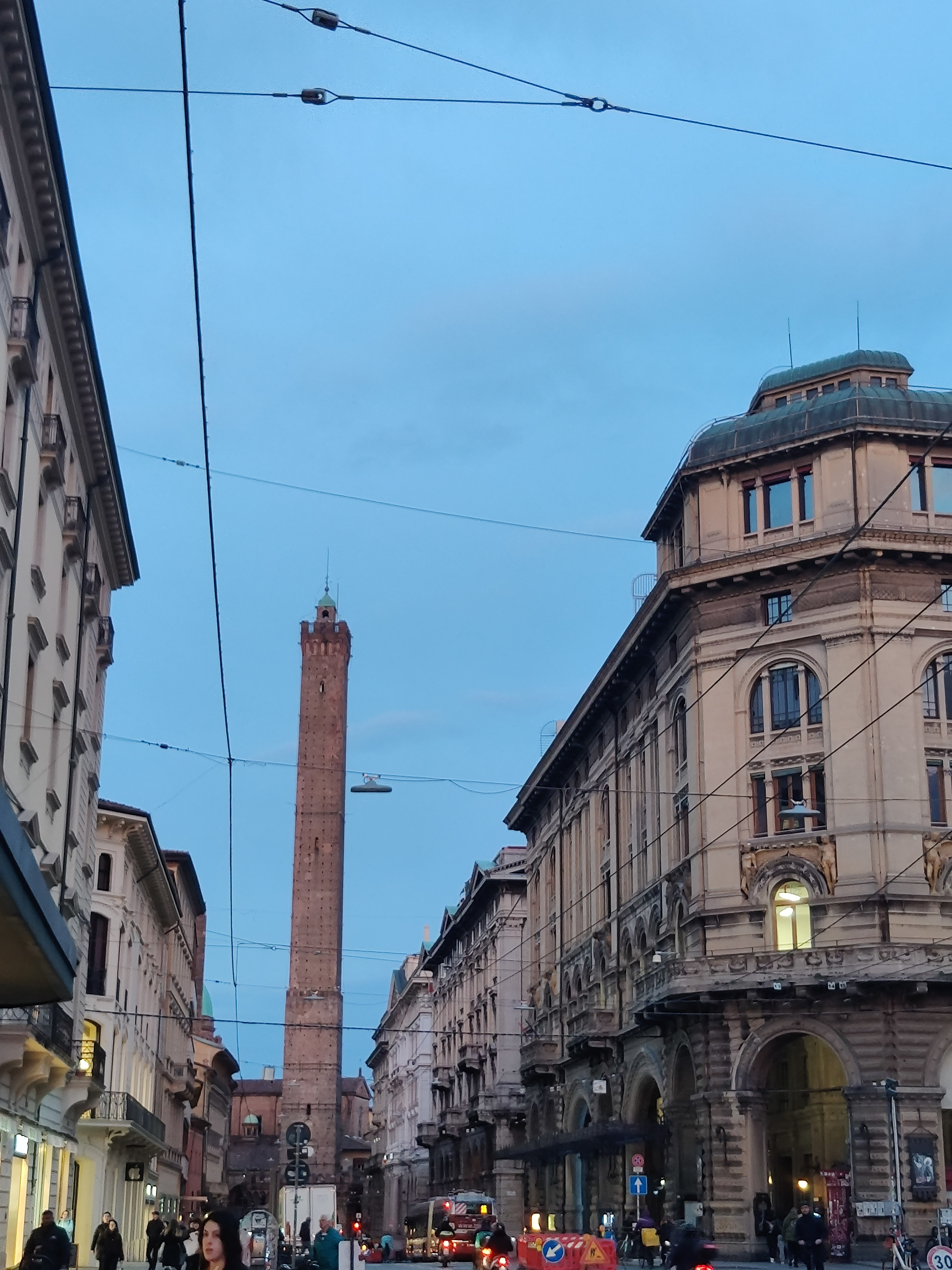 Bologna street at dusk with the medieval Due Torri towers rising above the rooftops