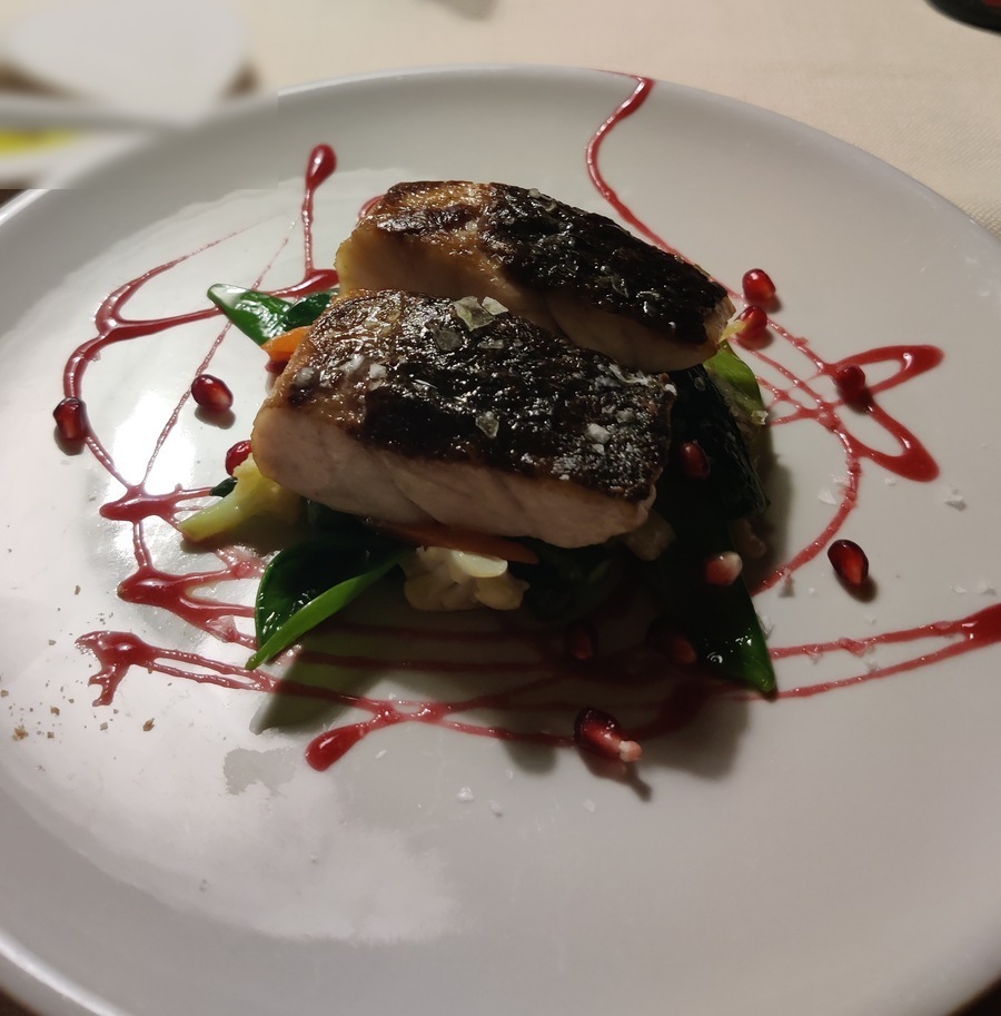Pan-seared fish with crispy skin, pomegranate sauce drizzle and seasonal vegetables on white plate