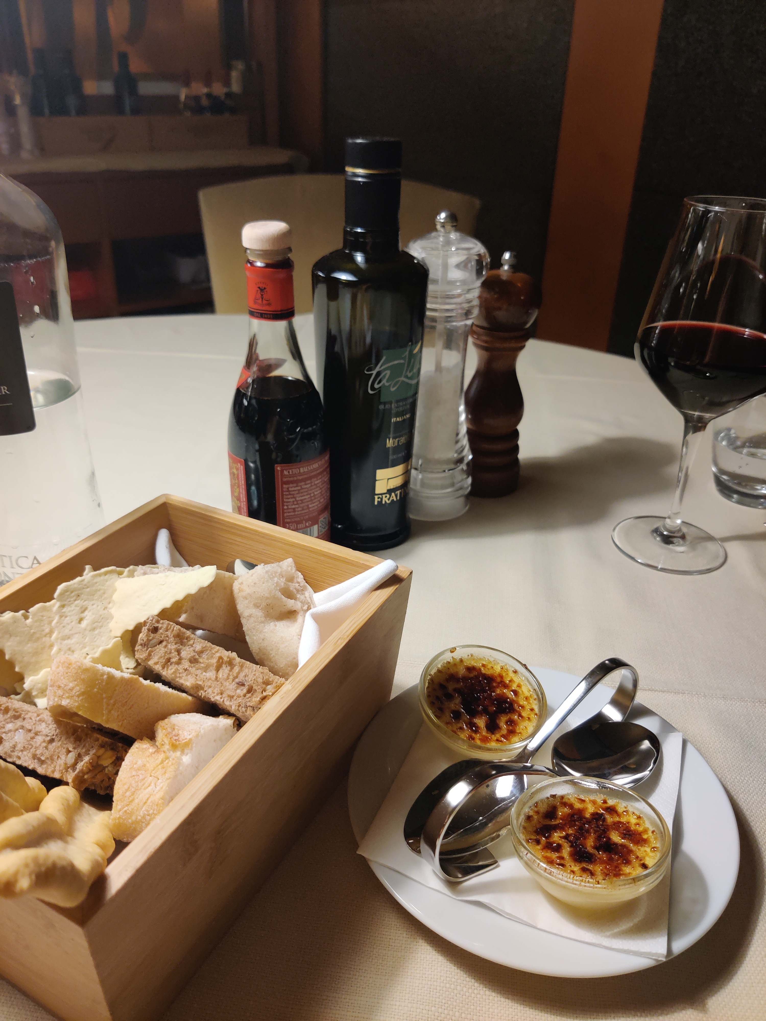 Restaurant table set with bread box, balsamic vinegar, olive oil, red wine and crème brûlée amuse-bouche