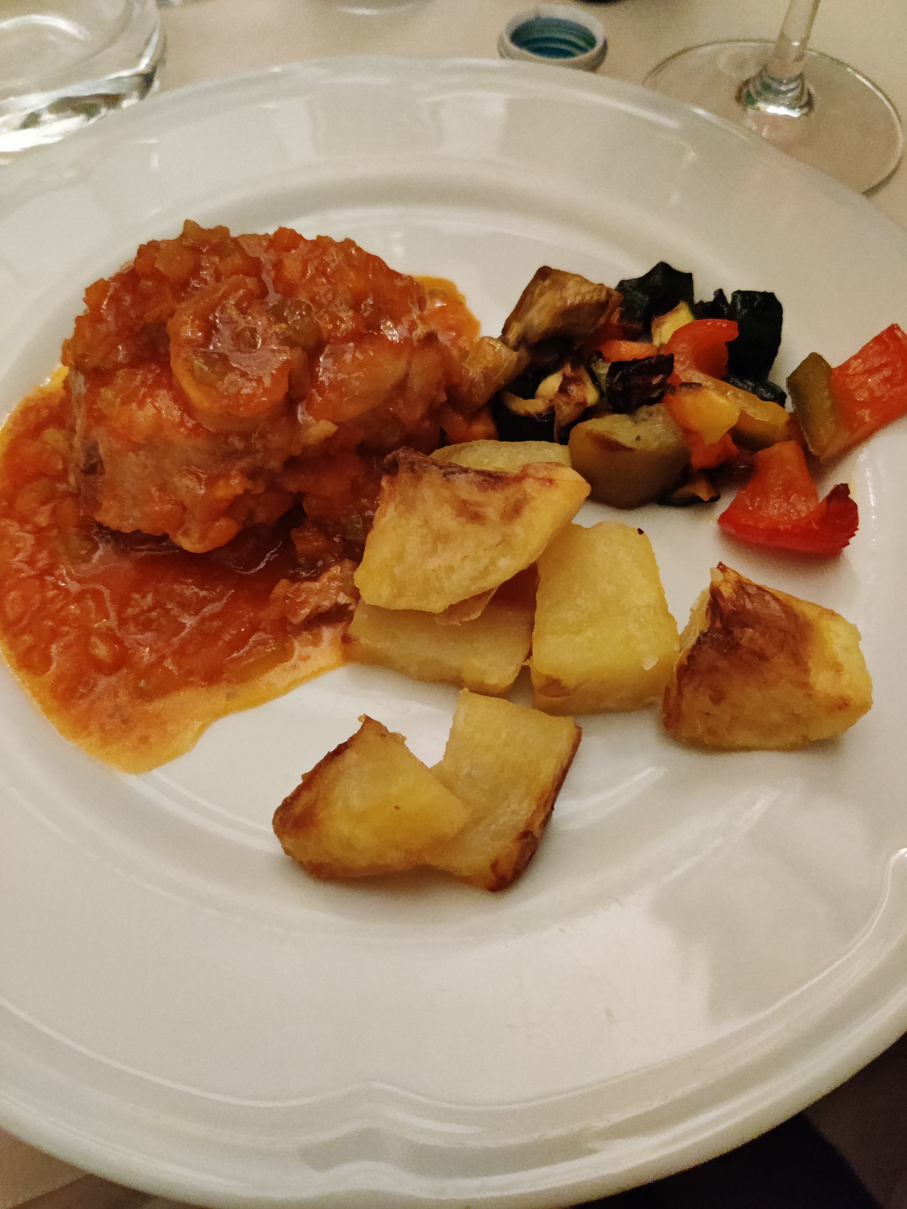 Main course of braised meat in rich tomato sauce with roasted potatoes and grilled seasonal vegetables