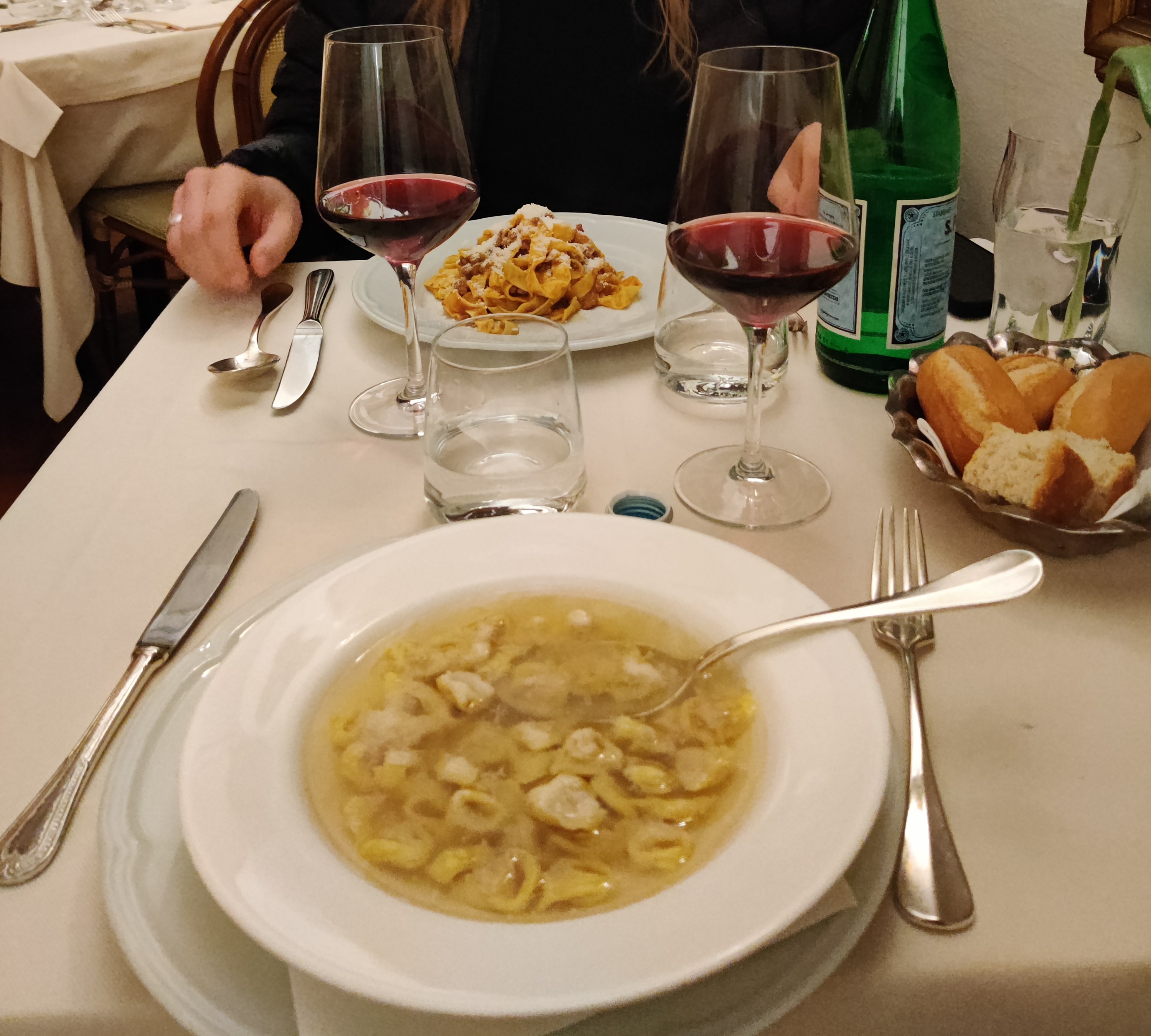 Restaurant table with Tortellini in Brodo in the foreground and Tagliatelle Ragù in the background, two glasses of red wine