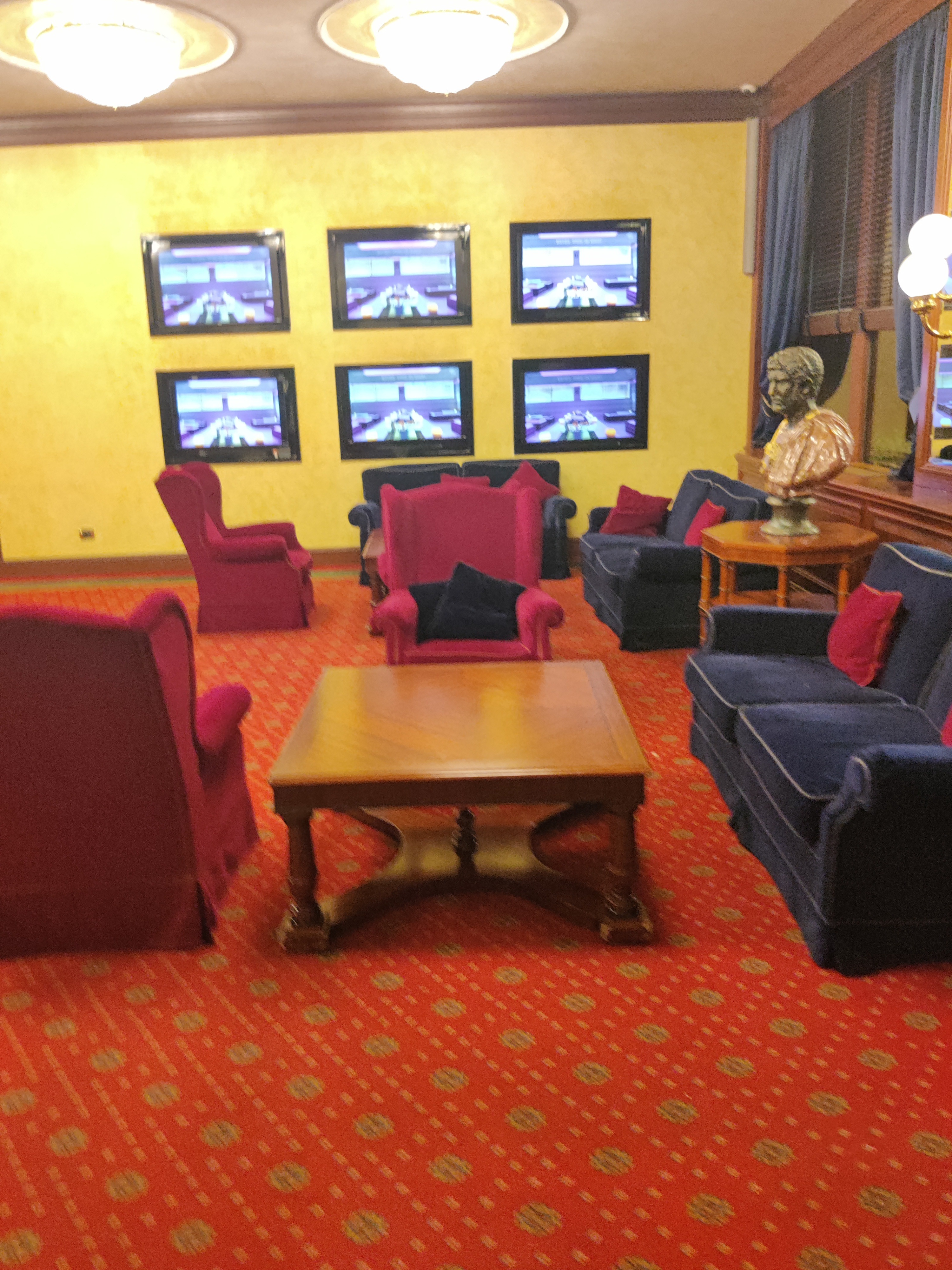 Hotel lounge with velvet armchairs and multiple framed screens on the wall