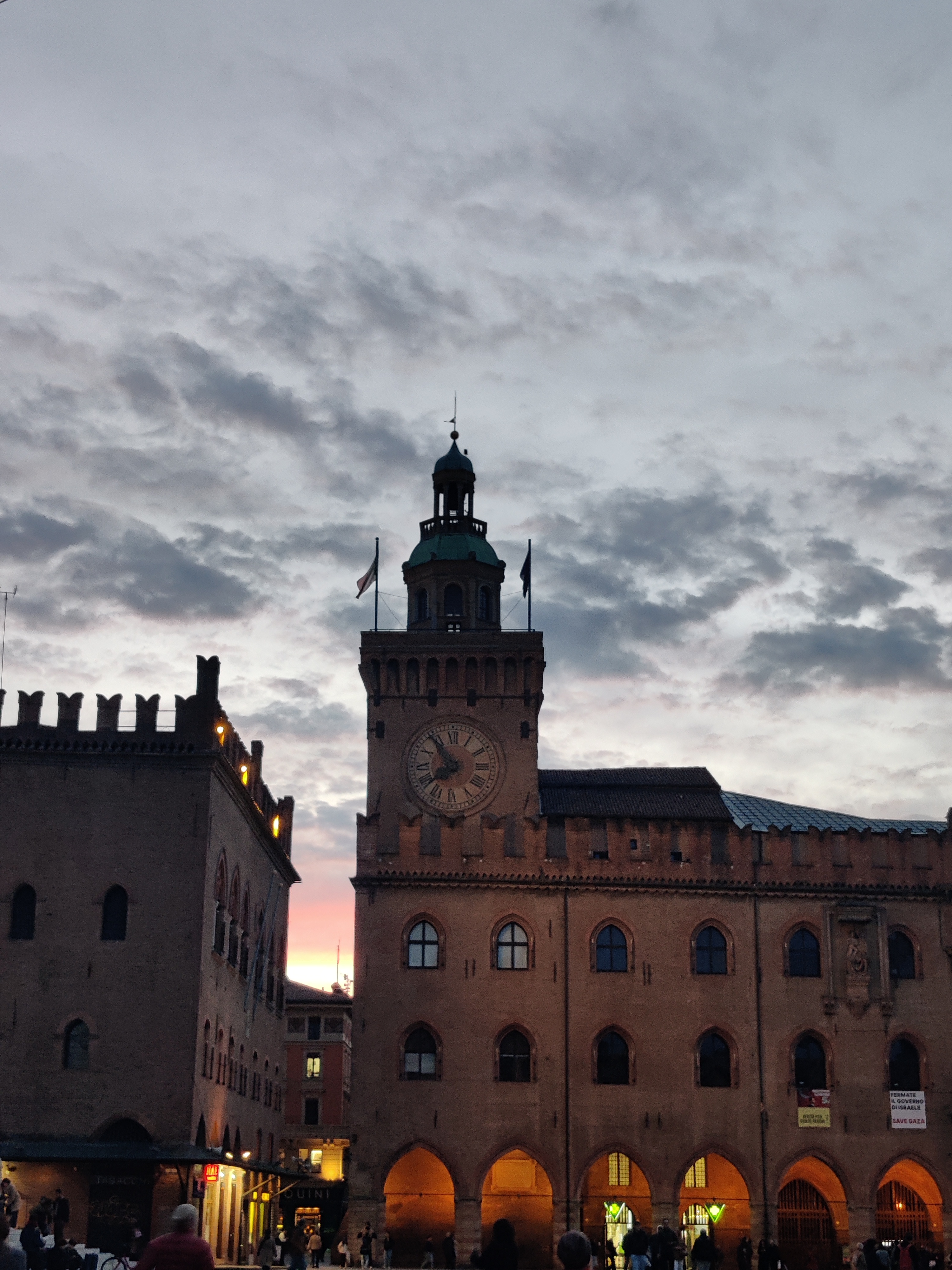 Palazzo d'Accursio clock tower at sunset over Piazza Maggiore with dramatic clouds