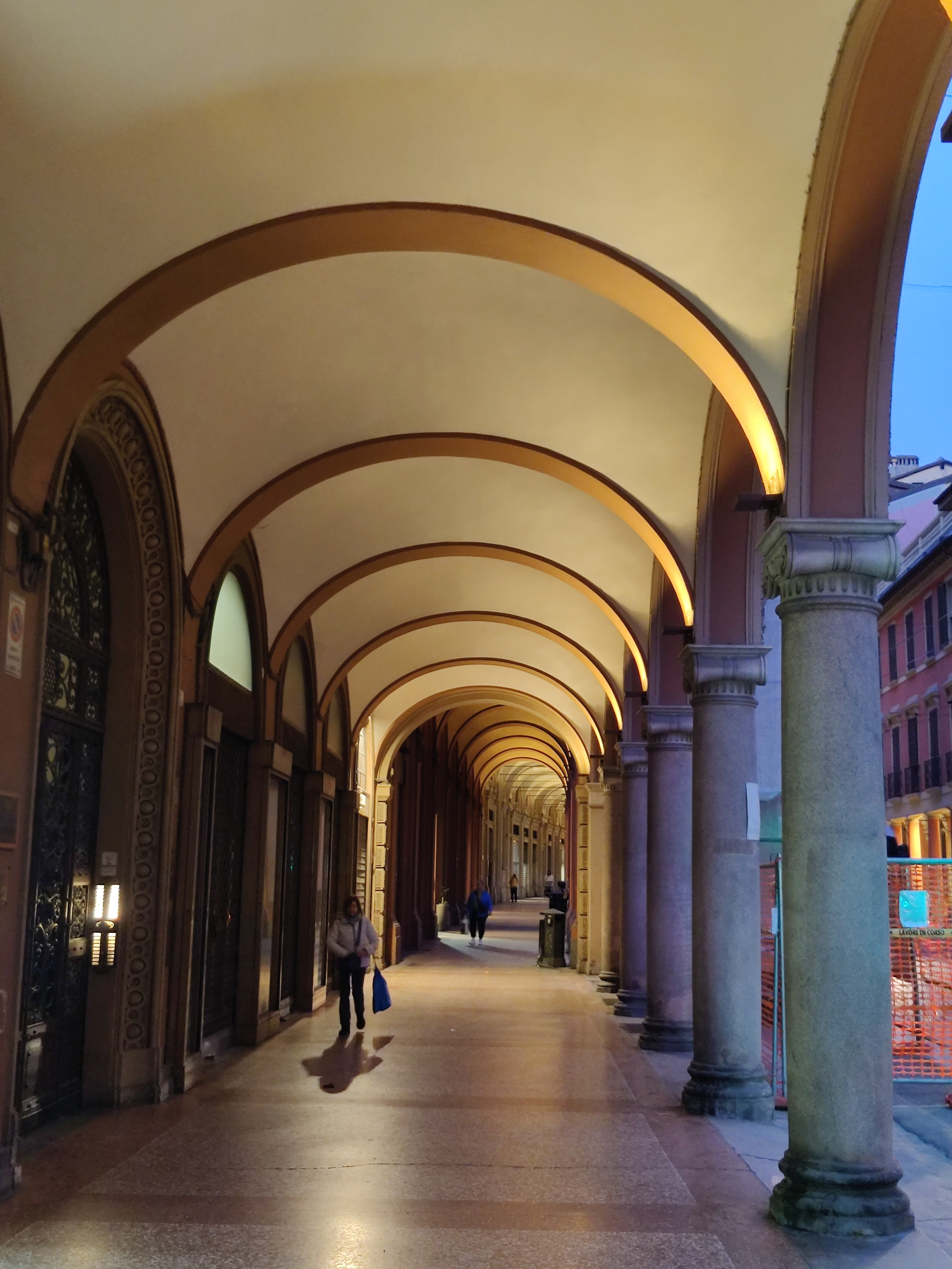 Warmly lit Bologna portico with repeating barrel-vaulted arches stretching into the distance
