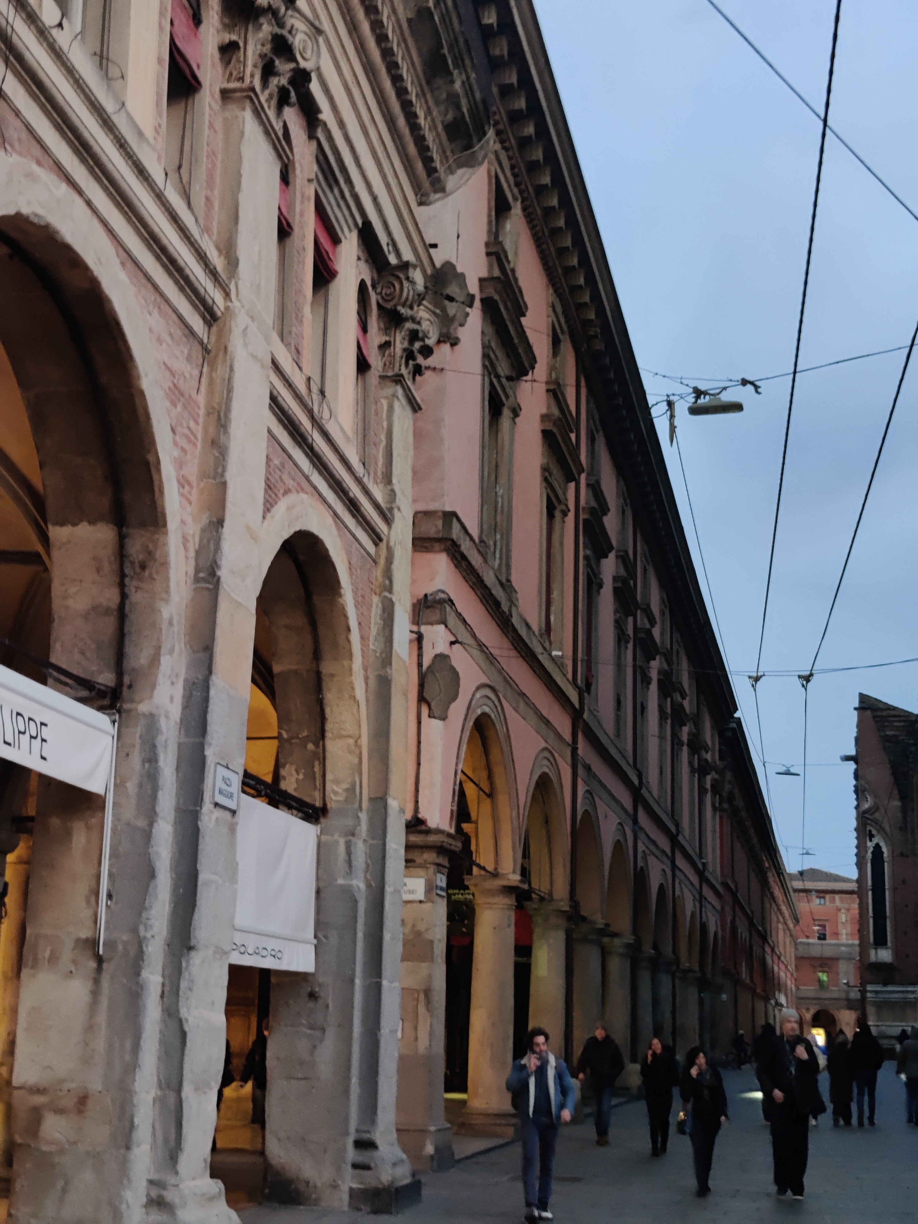 Long row of stone portico columns and arches lining a Bologna street at dusk
